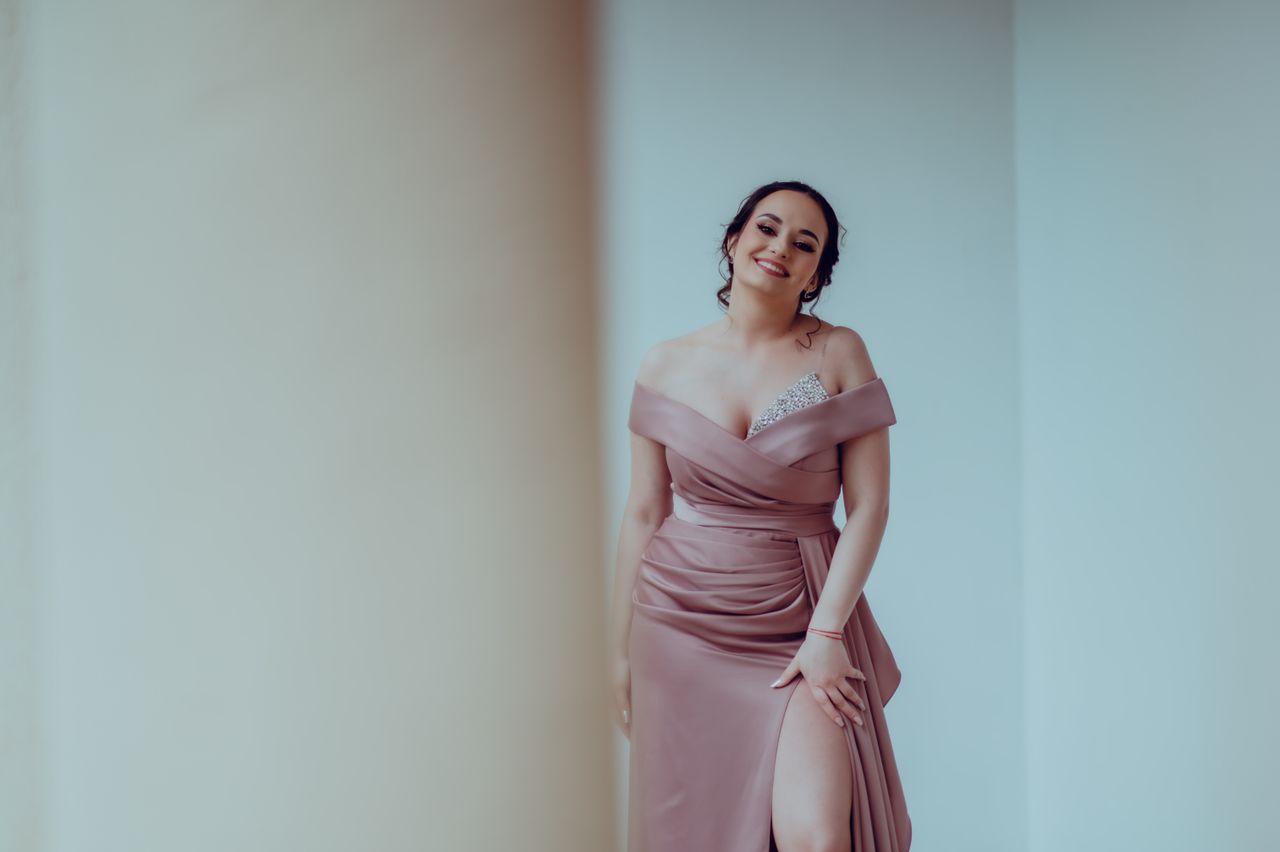 about-us-02 Elegant woman in a glamorous dress posing indoors with a joyful smile.